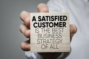 A wooden block that reads "A Satisfied Customer Is The Best Business Strategy of All"